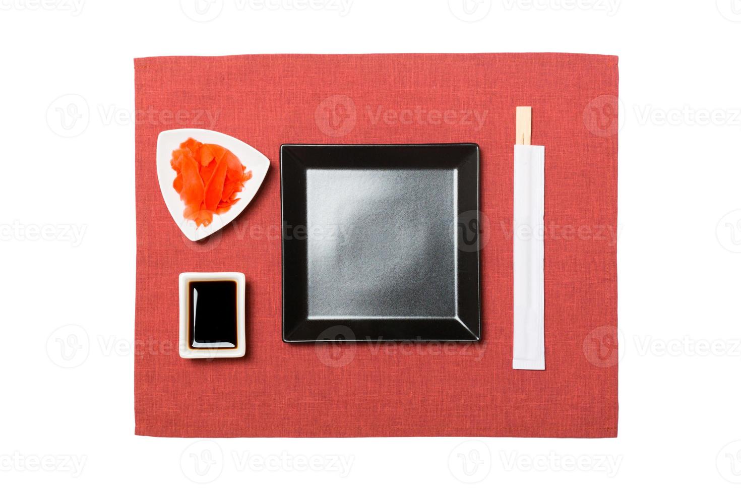 Empty black square plate with chopsticks for sushi, ginger and soy sauce on red napkin background. Top view with copy space for you design photo
