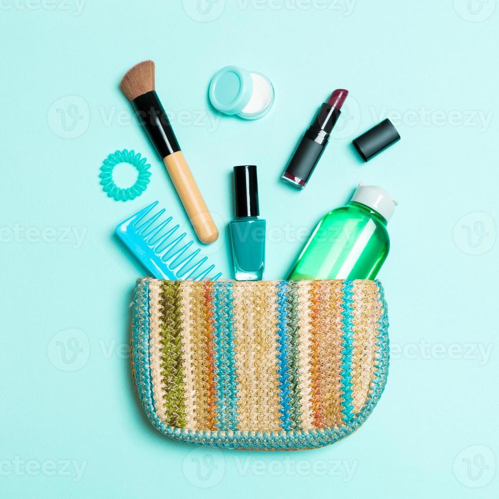 Make up products spilling out of cosmetics bag on blue pastel background with empty space for your design photo