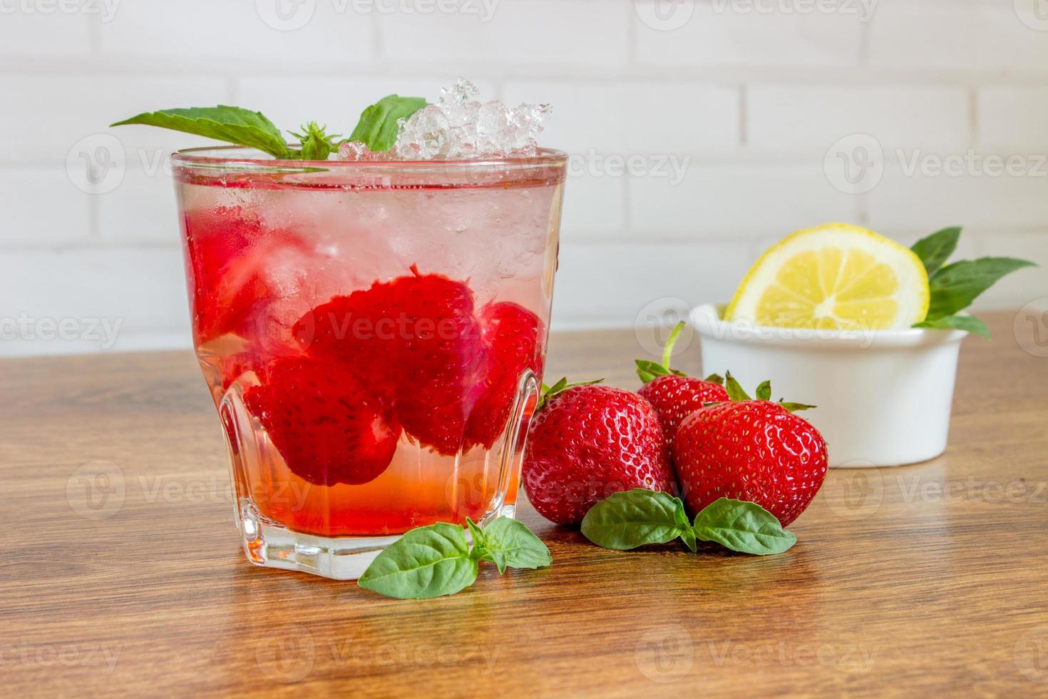 A refreshing summer drink with ice, strawberries and lemon on a wooden background. The concept of fruit drink. photo