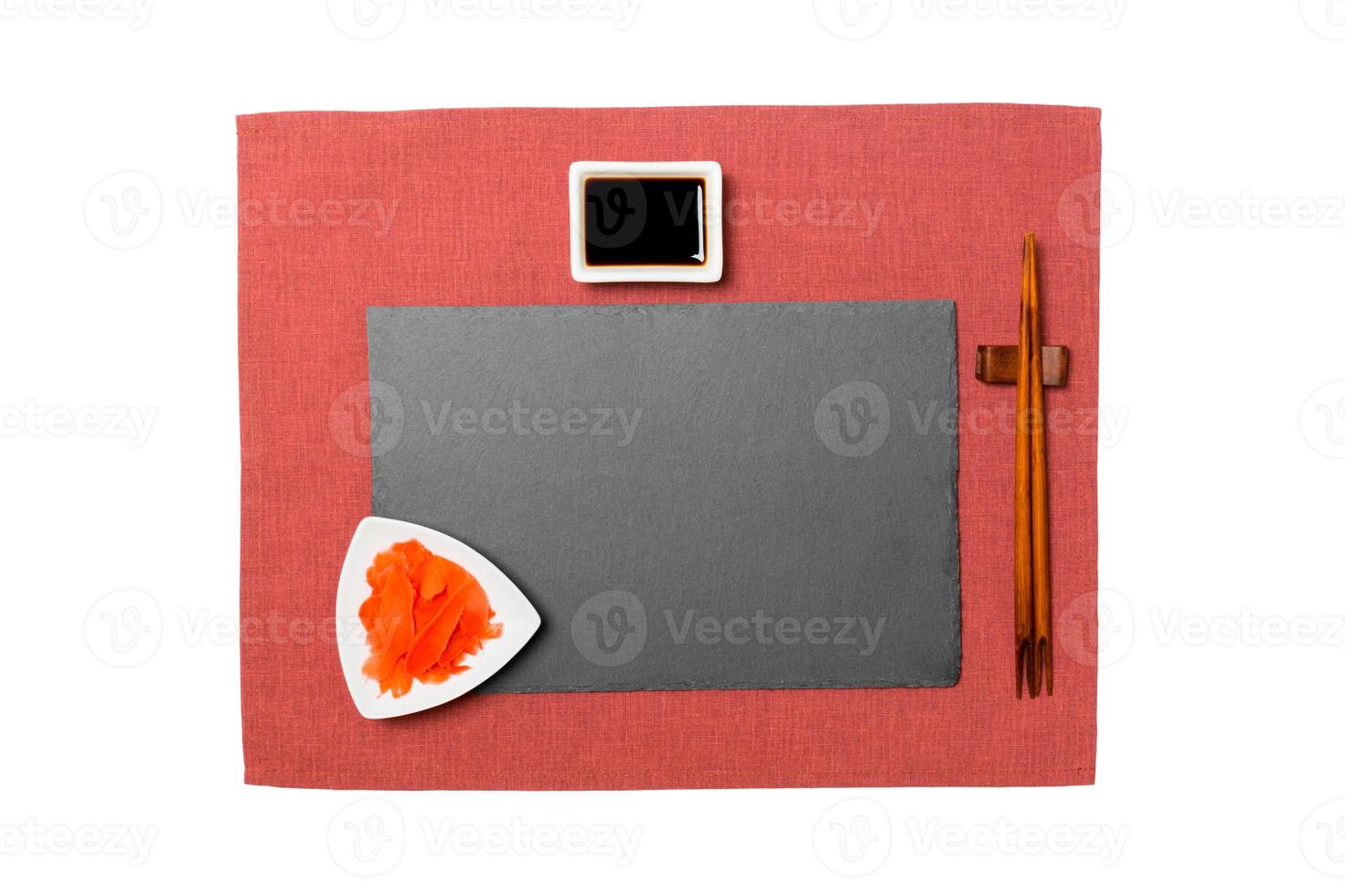 Empty rectangular black slate plate with chopsticks for sushi, ginger and soy sauce on red napkin background. Top view with copy space for you design photo
