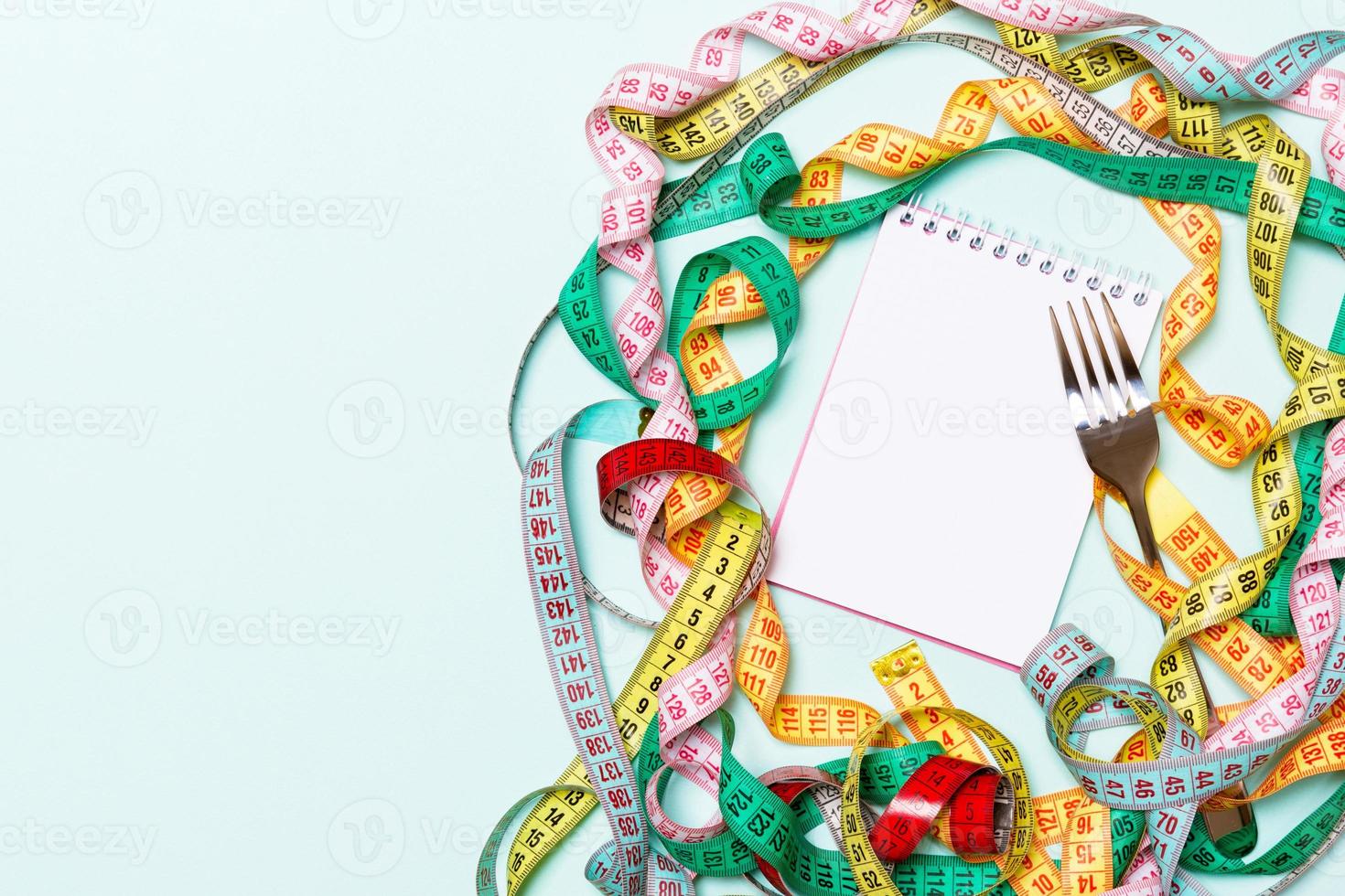 Top view of notebook with fork surrounded with colorful measuring tapes on blue background. Copy space with diet planning photo