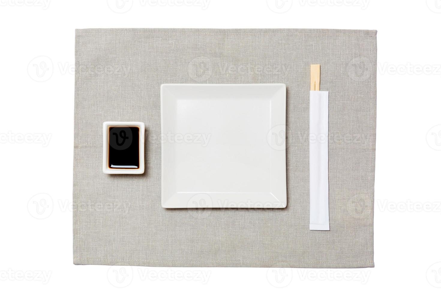 Empty white square plate with chopsticks for sushi and soy sauce on grey napkin background. Top view with copy space for you design photo