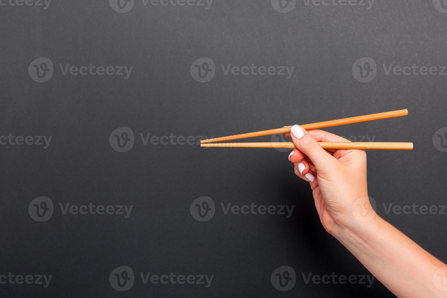 Wooden chopsticks in female hand on black background with empty space for your idea. Tasty food concept photo