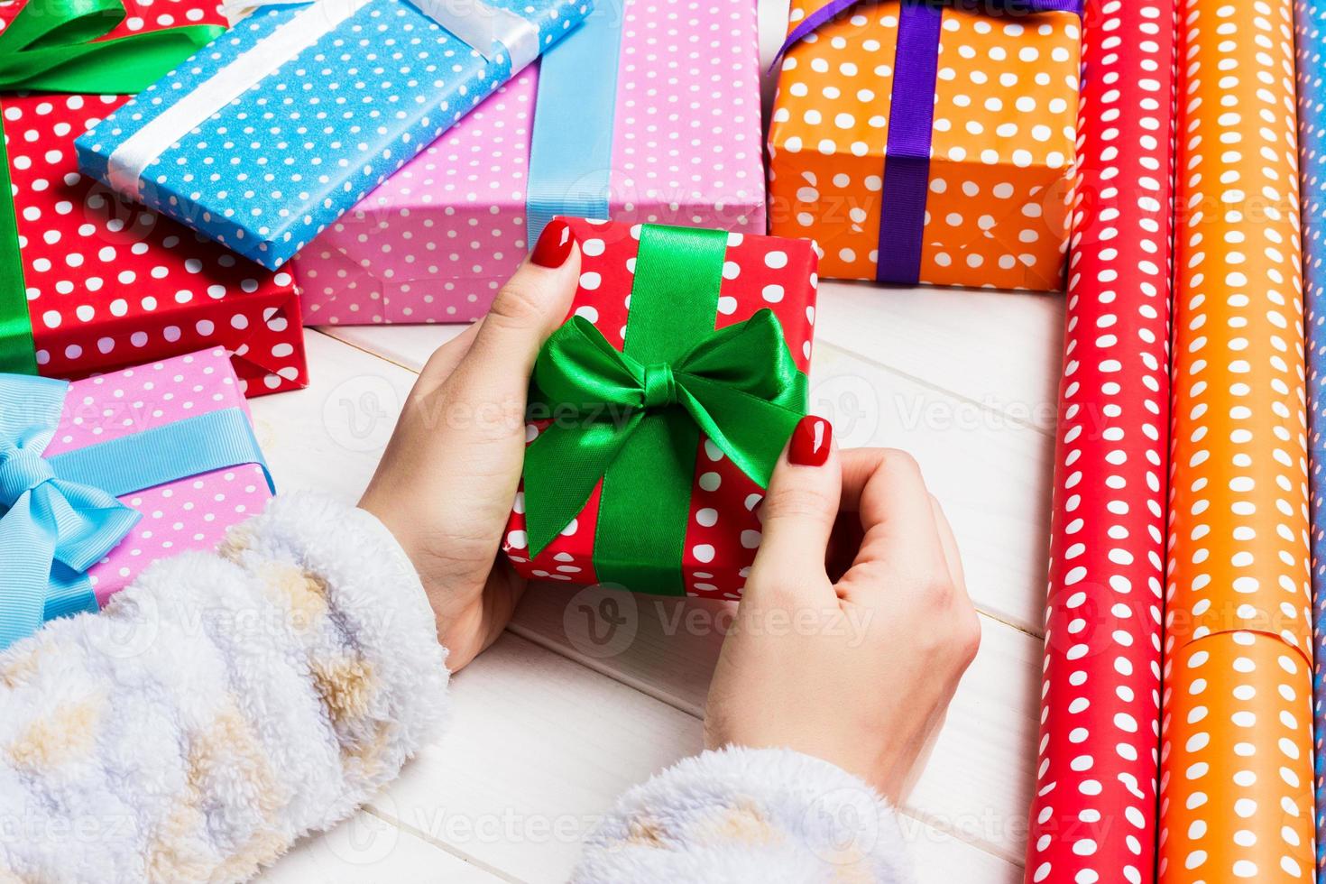 Top view of female hand tie up New Year present on festive wooden background. Gift boxes and rolled up wrapping paper. Christmas time concept photo