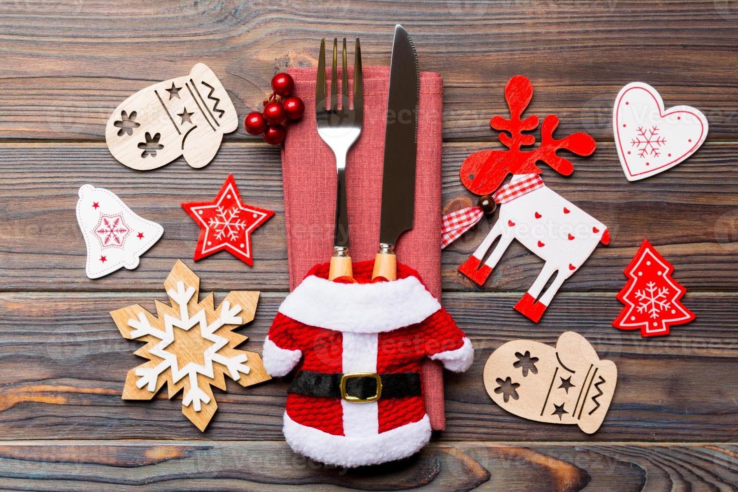 Top view of new year utensils on napkin with holiday decorations and reindeer on wooden background. Close up of christmas dinner concept photo