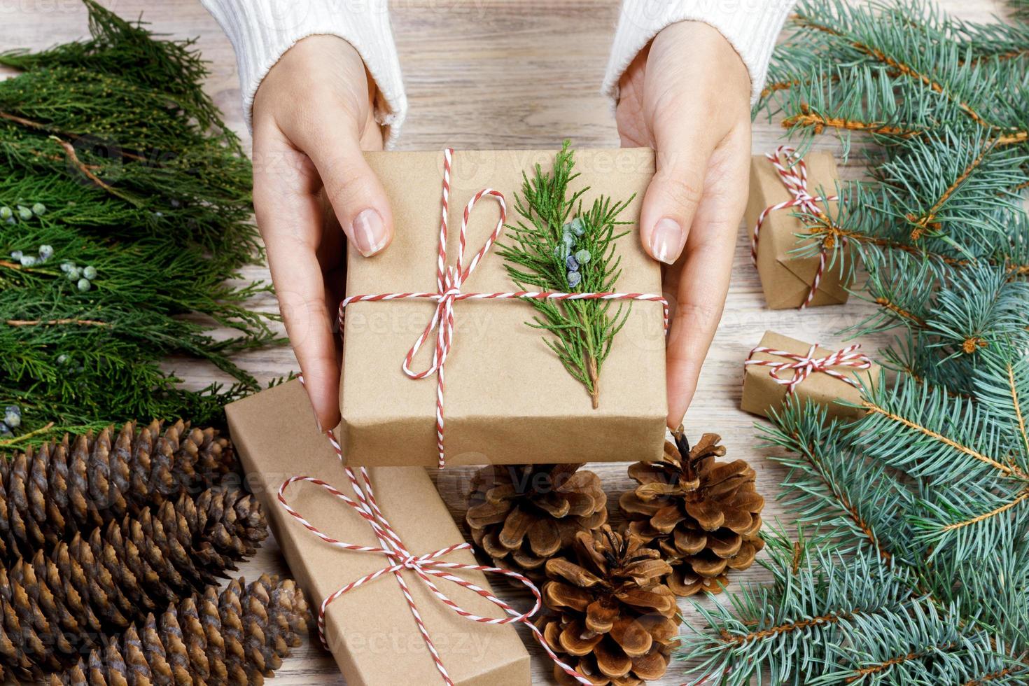 manos femeninas envolviendo regalos de navidad en papel y atándolos con hilos rojos foto