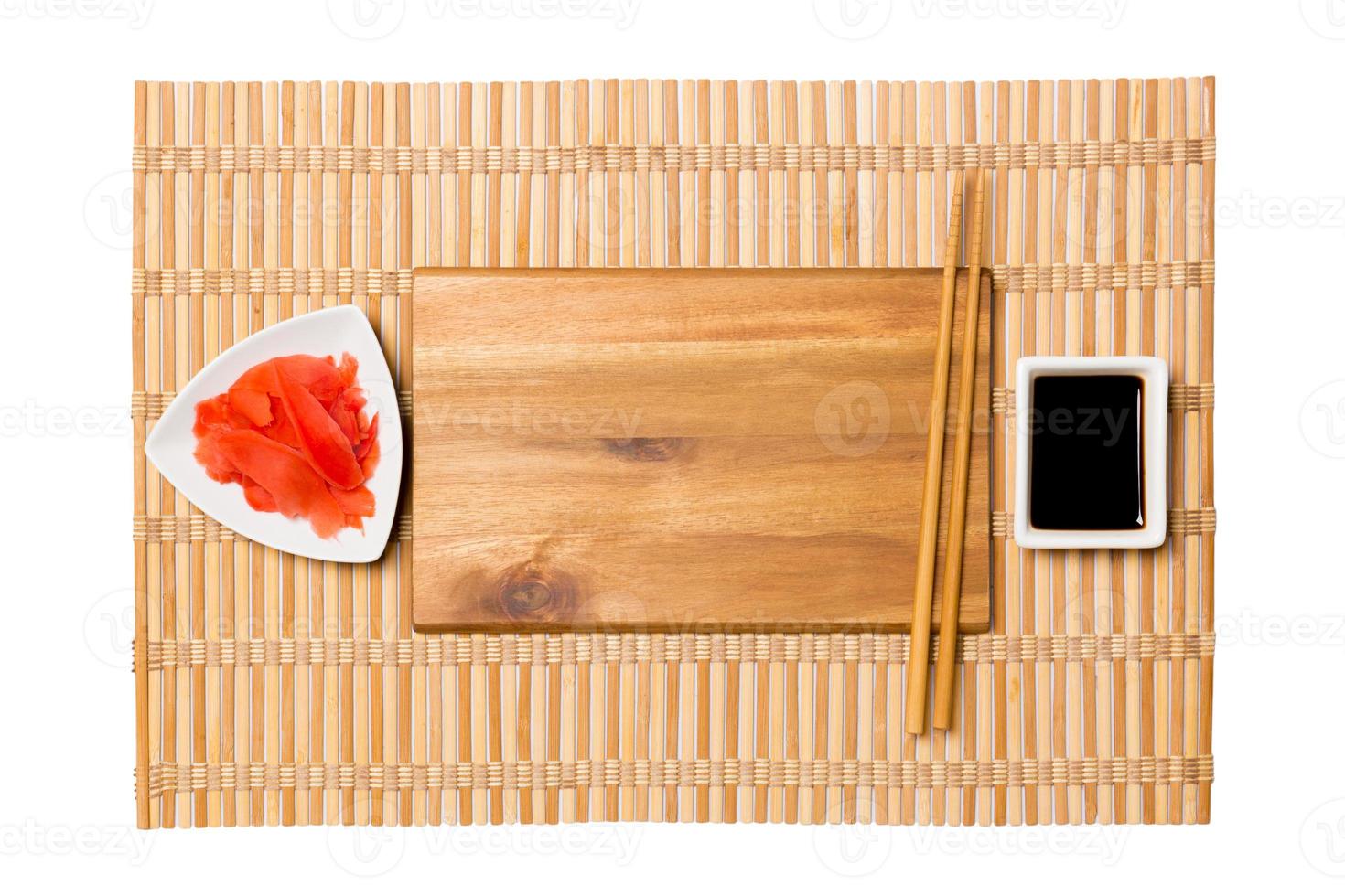 Empty rectangular brown wooden plate with chopsticks for sushi and soy sauce, ginger on yellow bamboo mat background. Top view with copy space for you design photo