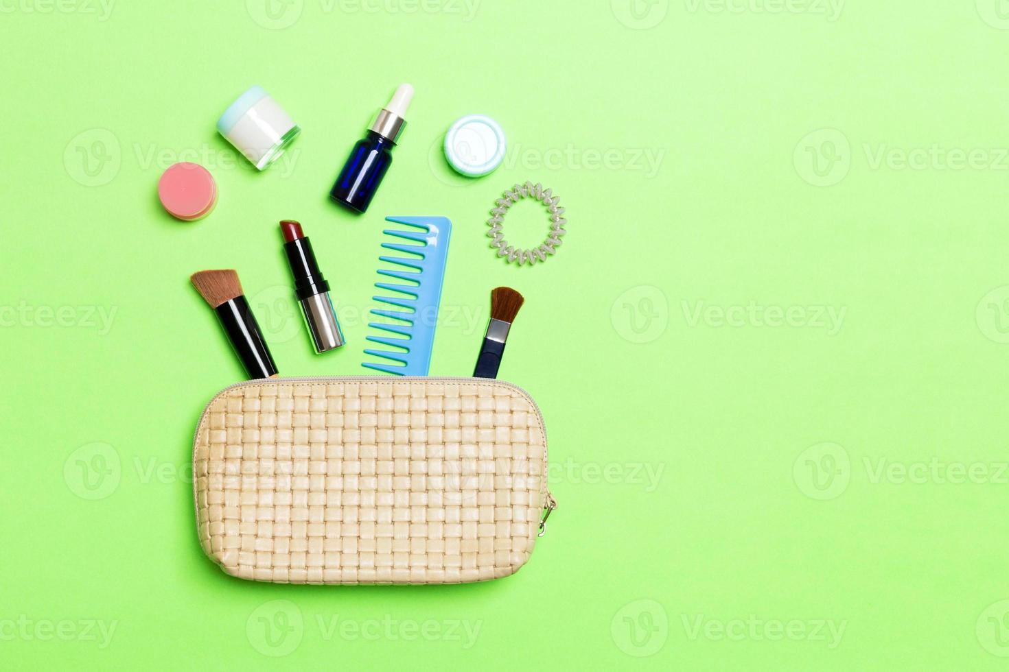 Aerial view of a leather cosmetics bag with make up beauty products spilling out on green background. Beautiful skin concept with copy space photo