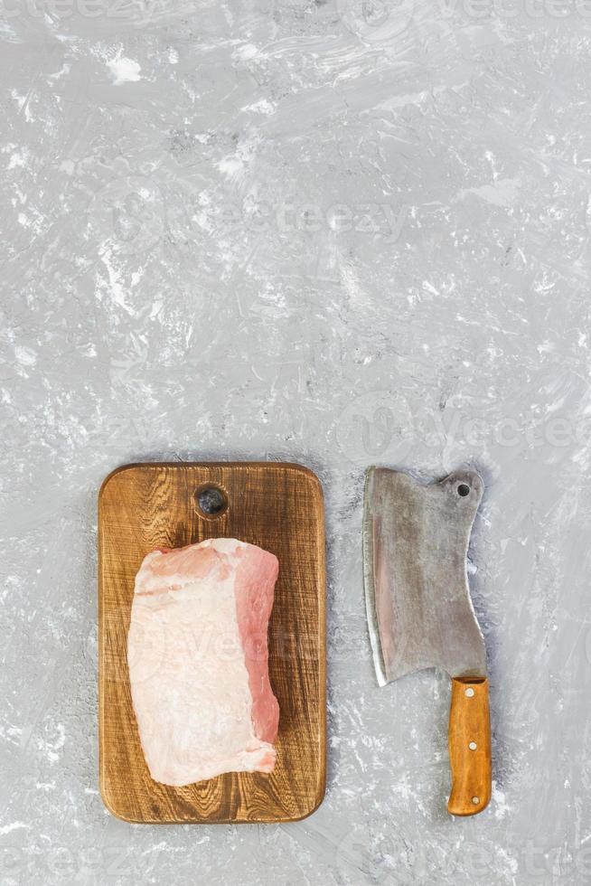 corte crudo de paleta de cerdo a bordo con cuchillo o hacha de cocina. Cuchilla con carne cruda fresca sobre fondo de hormigón gris foto