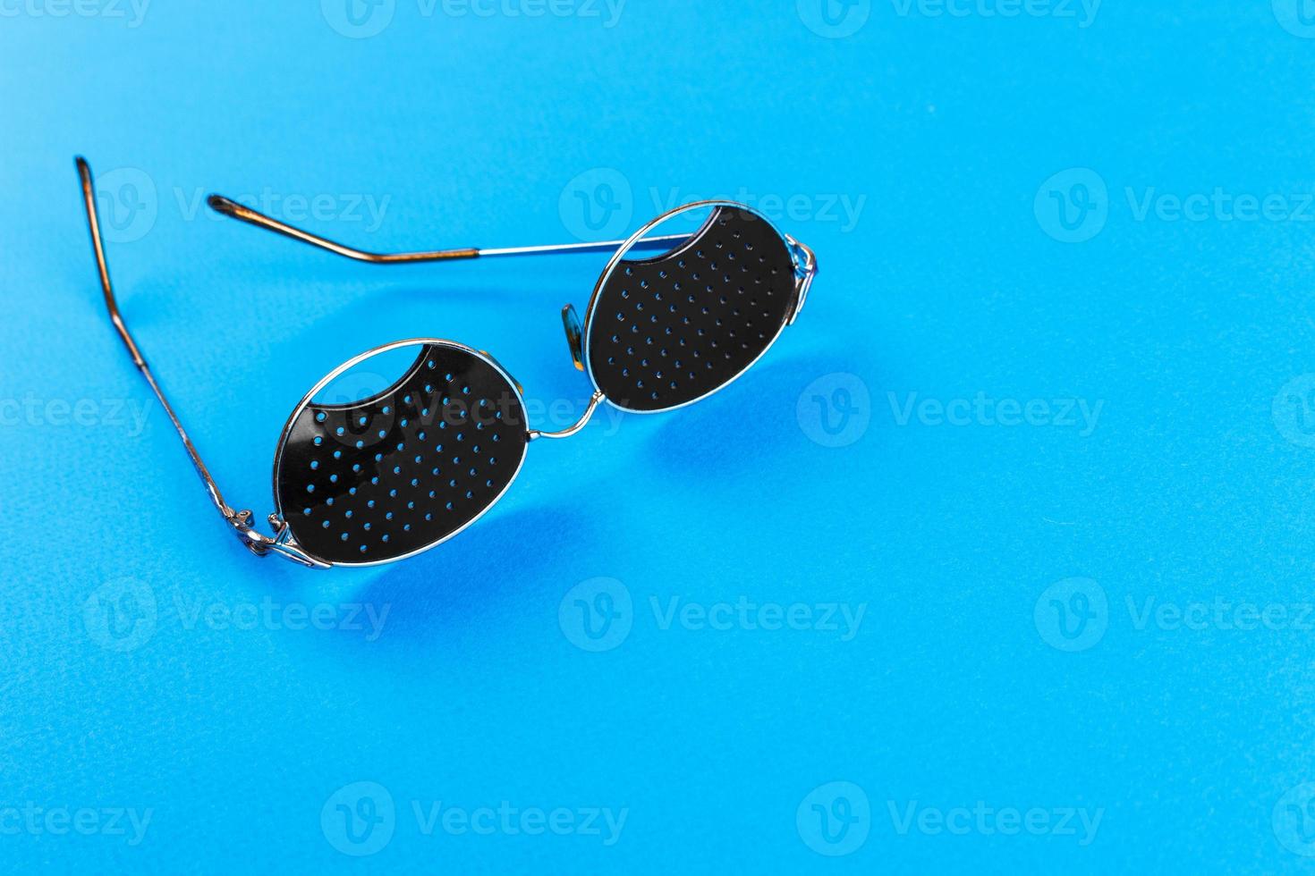 Black pinhole glasses on blue background. Medical concept. Top view photo