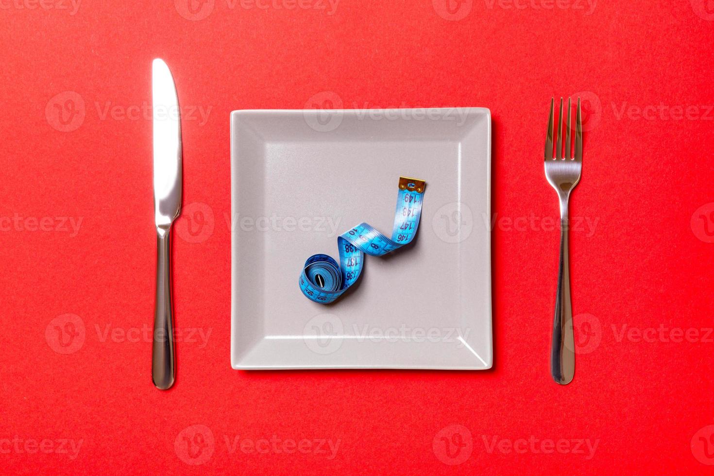 Measuring tape in a plate with fork and knife on both sides on red background. Top view of weight loss concept photo