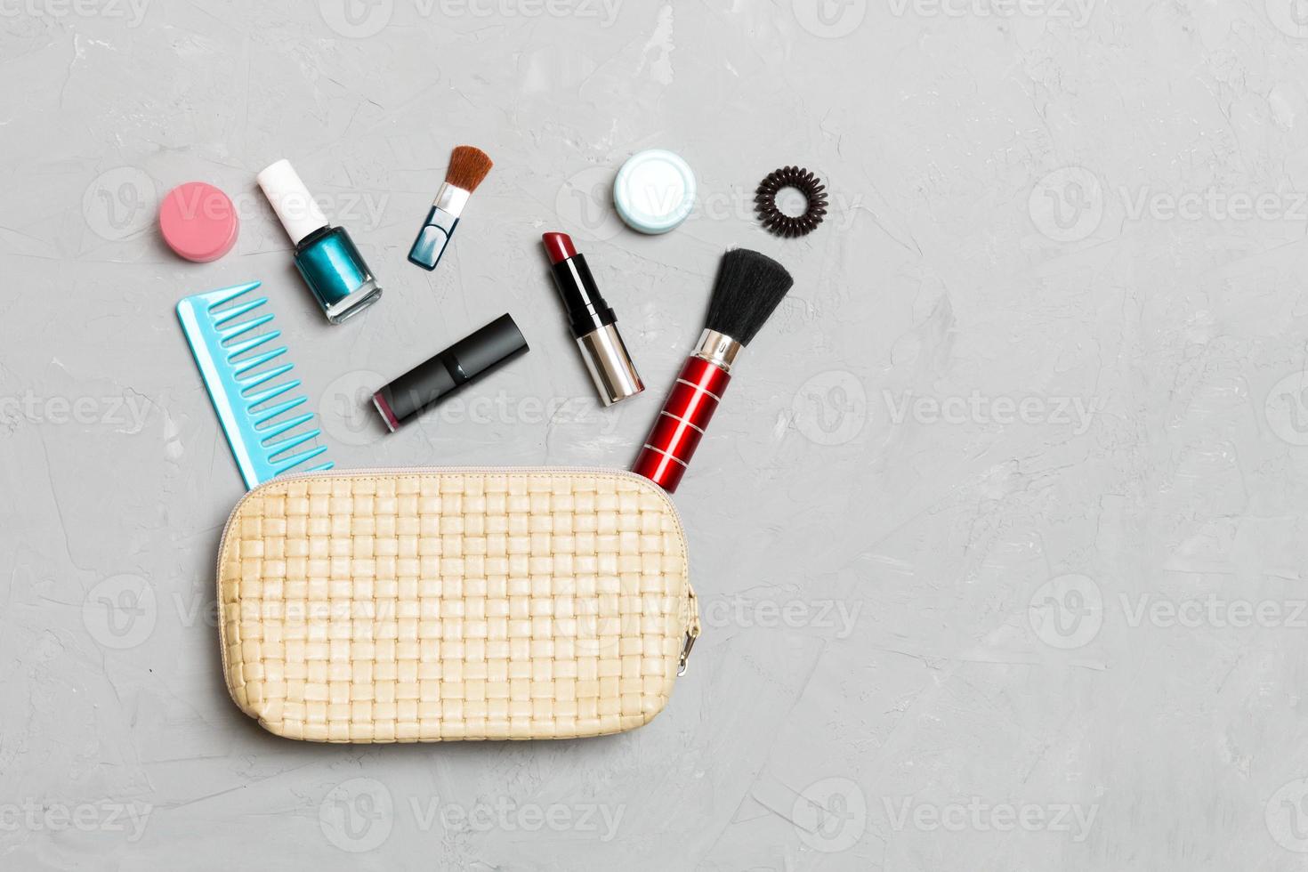 Top view of set of make up and skin care products spilling out of cosmetics bag on cement background. Beauty concept photo