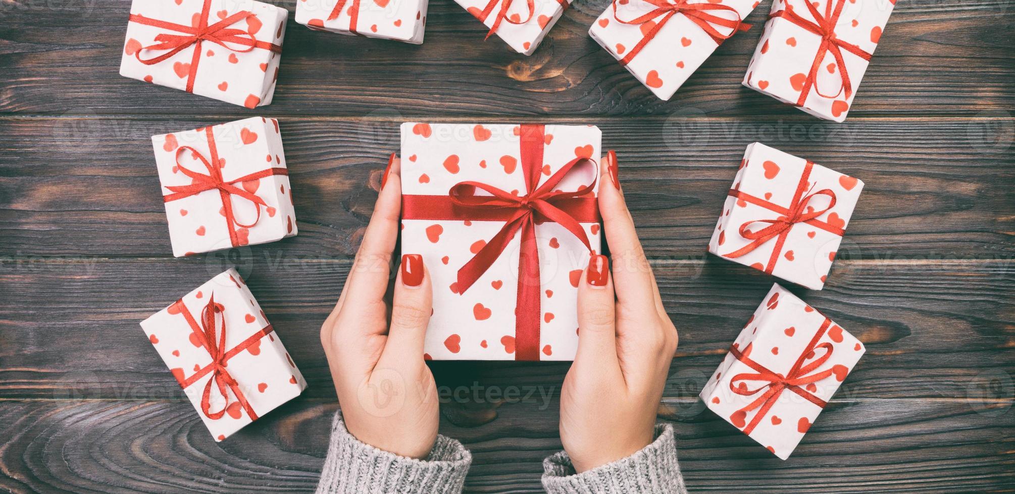 Woman hands giving Holidays gift box on wood table, Present box, red heart decoration of gift on wooden table, top view with copy space for you design. Toned web banner photo