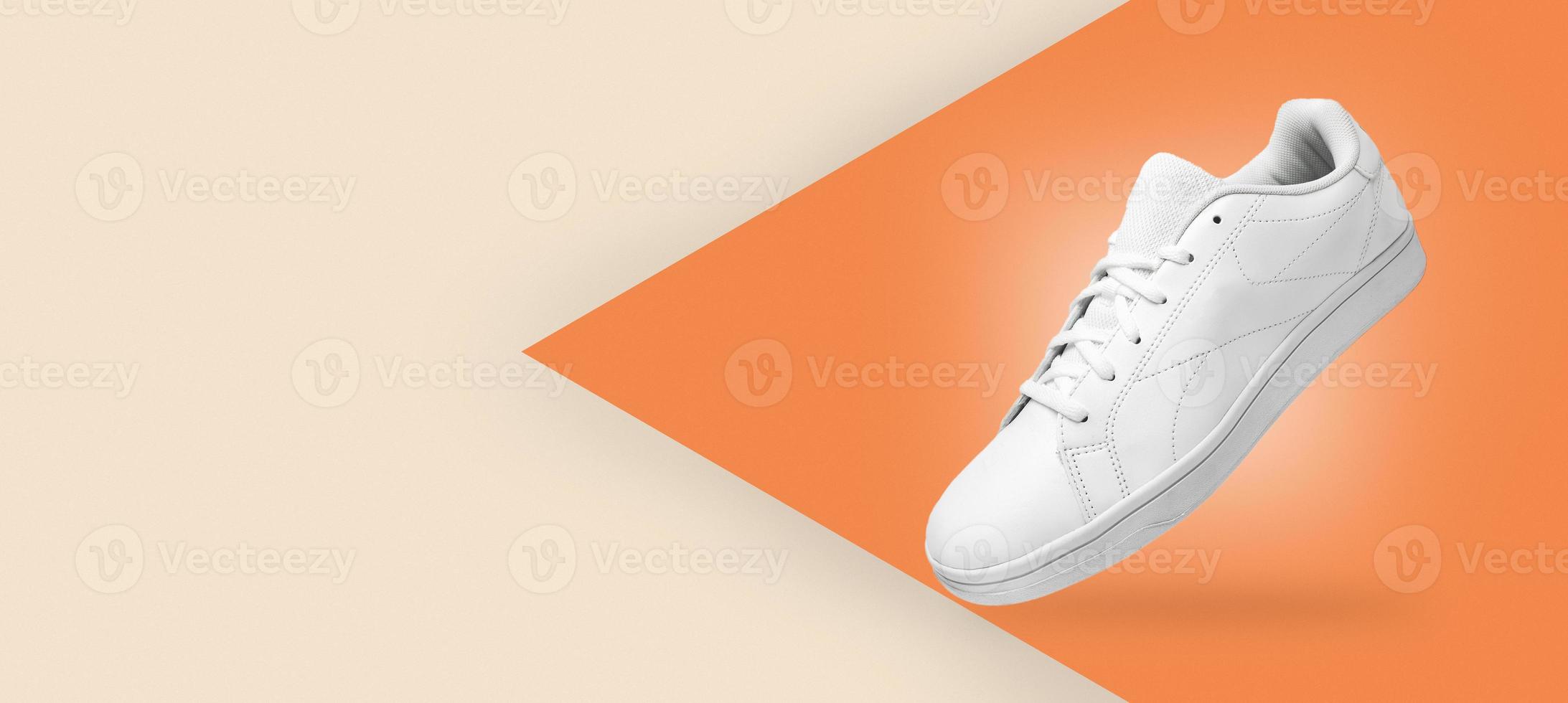 Banner with new pair of white sneakers isolated on light yellow and orange background. Sportive pair of shoes for mockup. Fashionable stylish sports casual shoes. photo