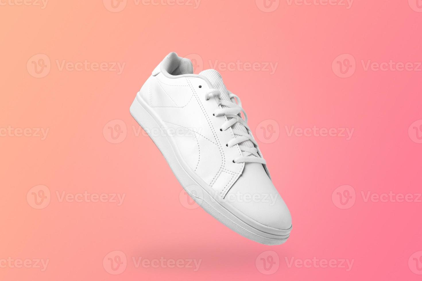 High angle view of white sneaker isolated on peachy background. Sportive pair of shoes for mockup. Fashionable stylish sports casual shoes. photo
