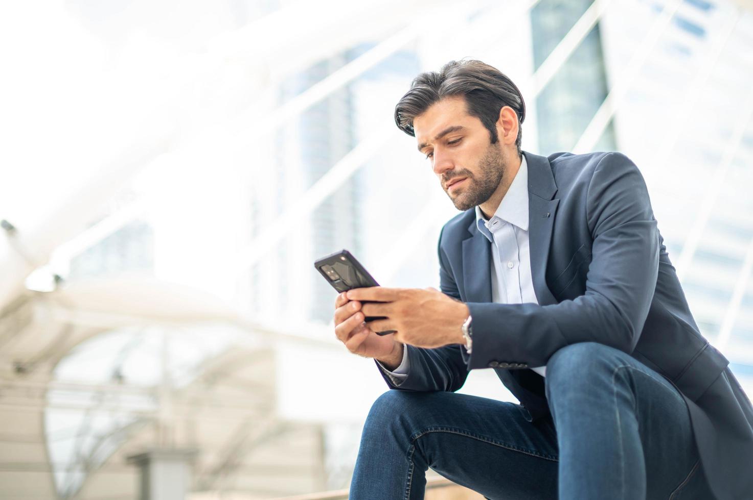 Closeup of young caucasian serious man using modern smartphone device while sitting at the public area, while looking at the social network on smartphone. photo