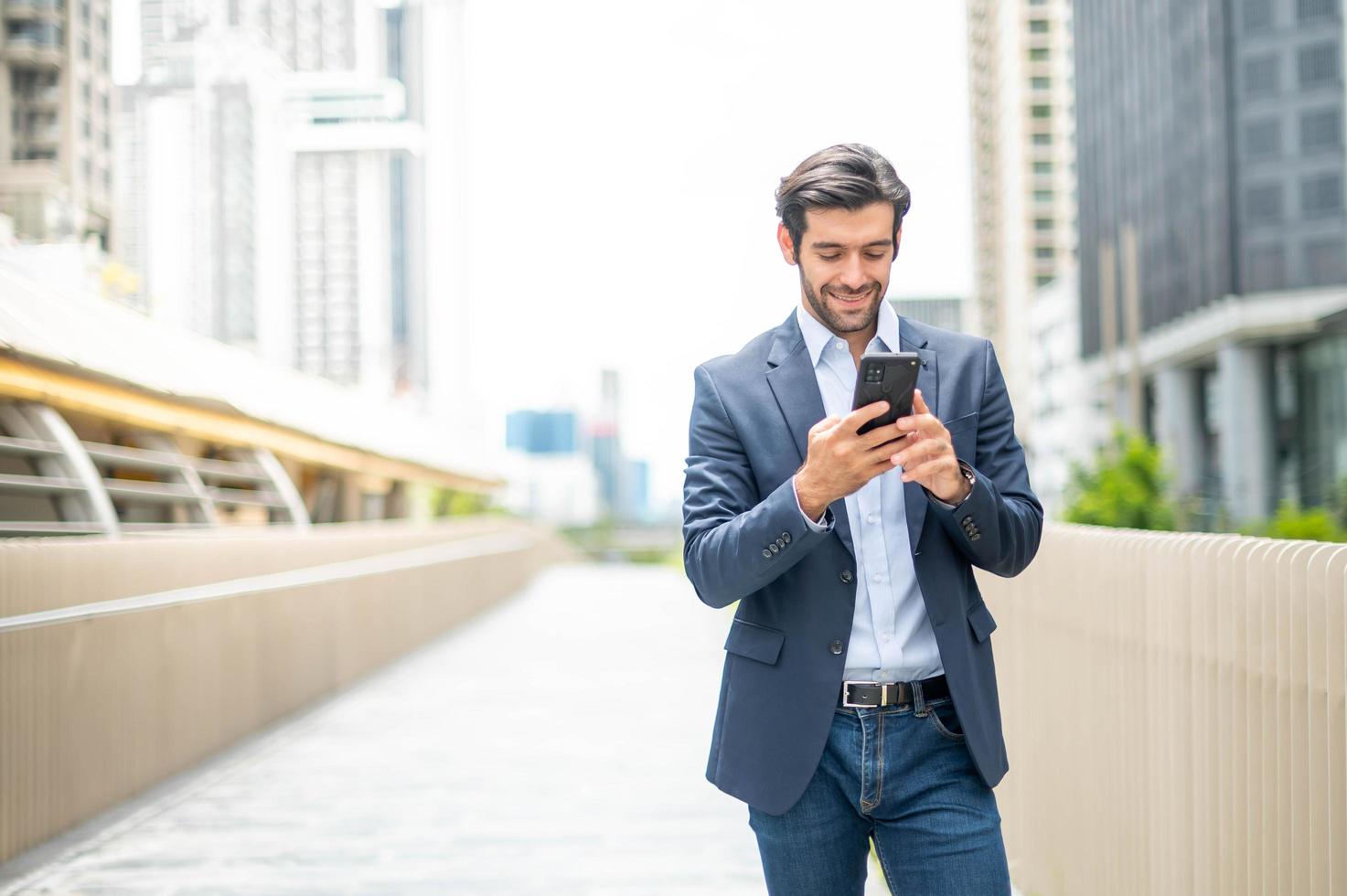The businessman uses smart phone for communicate with his friend while he walking at the putside. Feeling happy and relaxing, Casual young businessman wearing suit jacket. photo