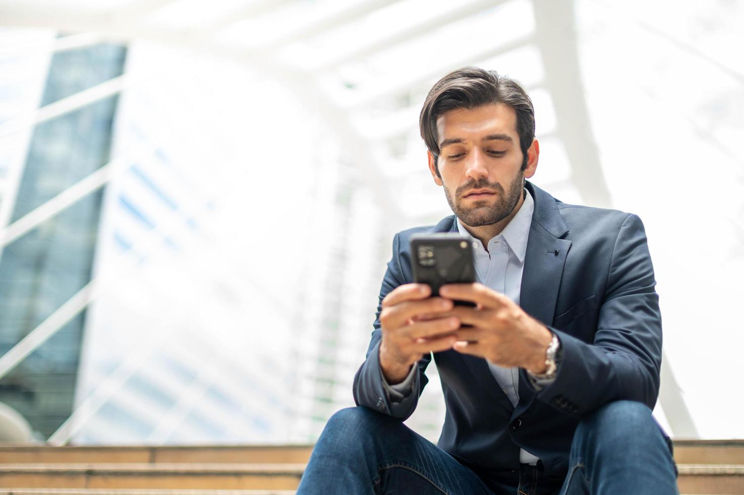 Closeup of young caucasian serious man using modern smartphone device while sitting at the public area, while looking at the social network on smartphone. photo