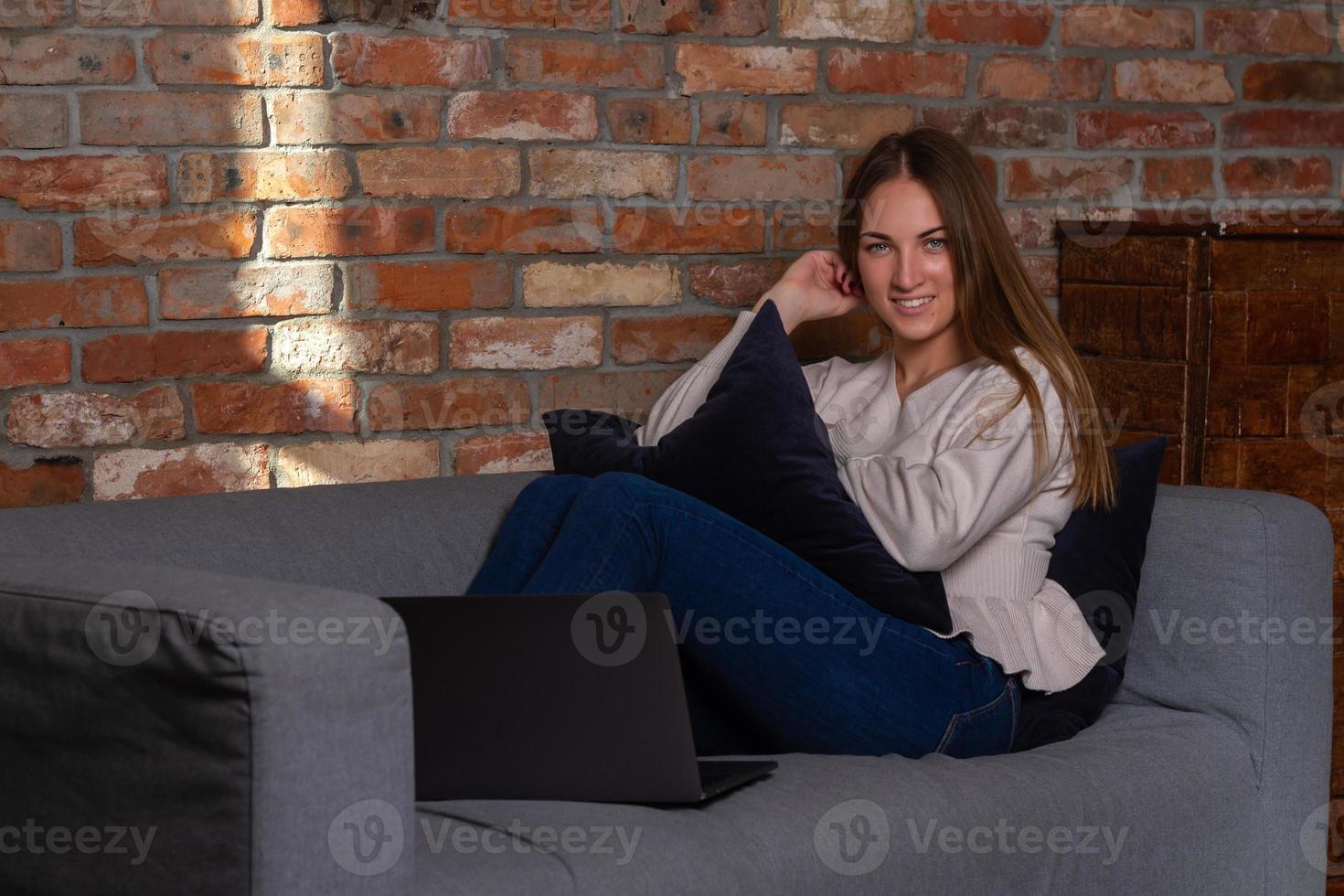 Smiling woman on a couch with a laptop in front of her photo