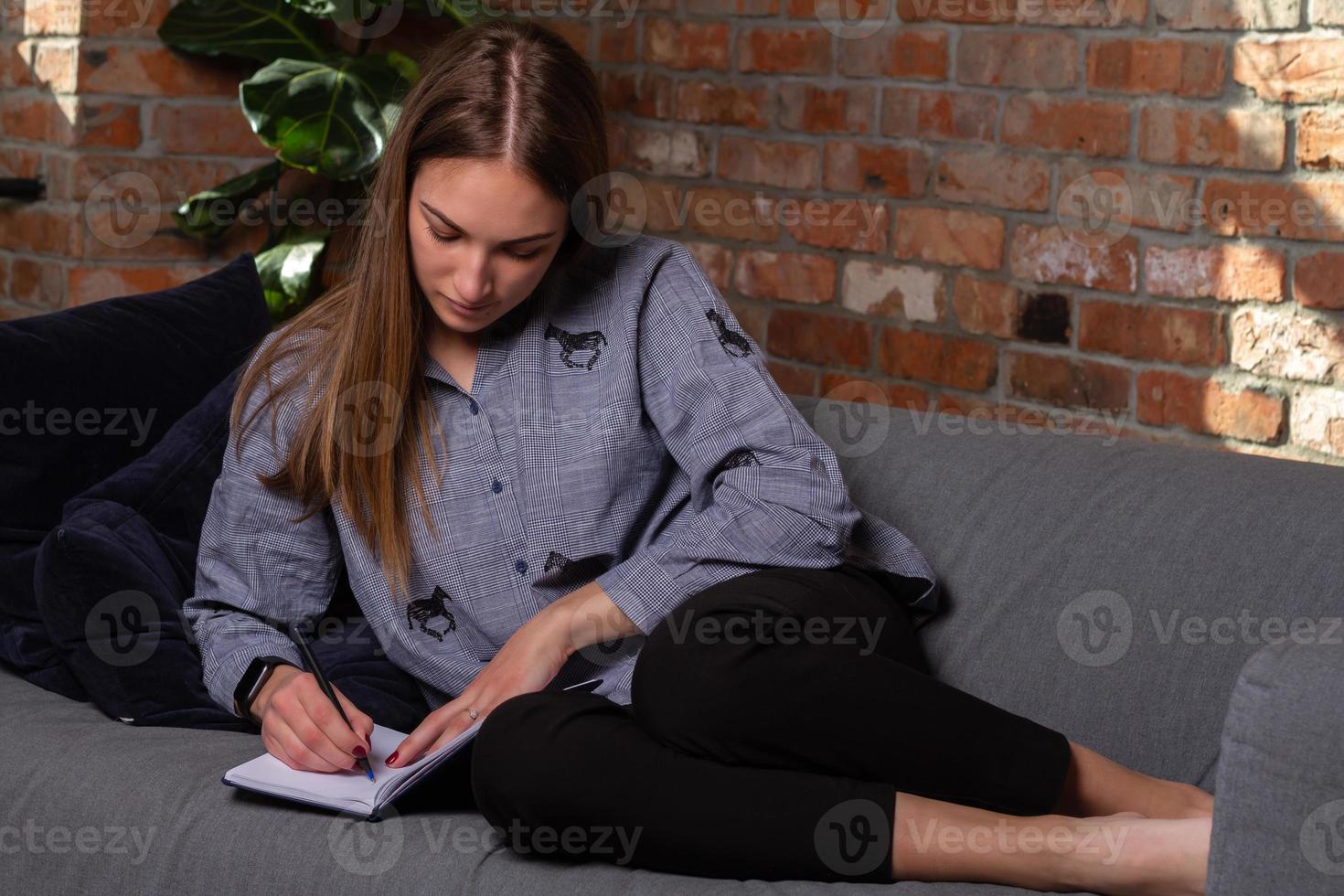 mujer en el sofá escribiendo en un cuaderno foto