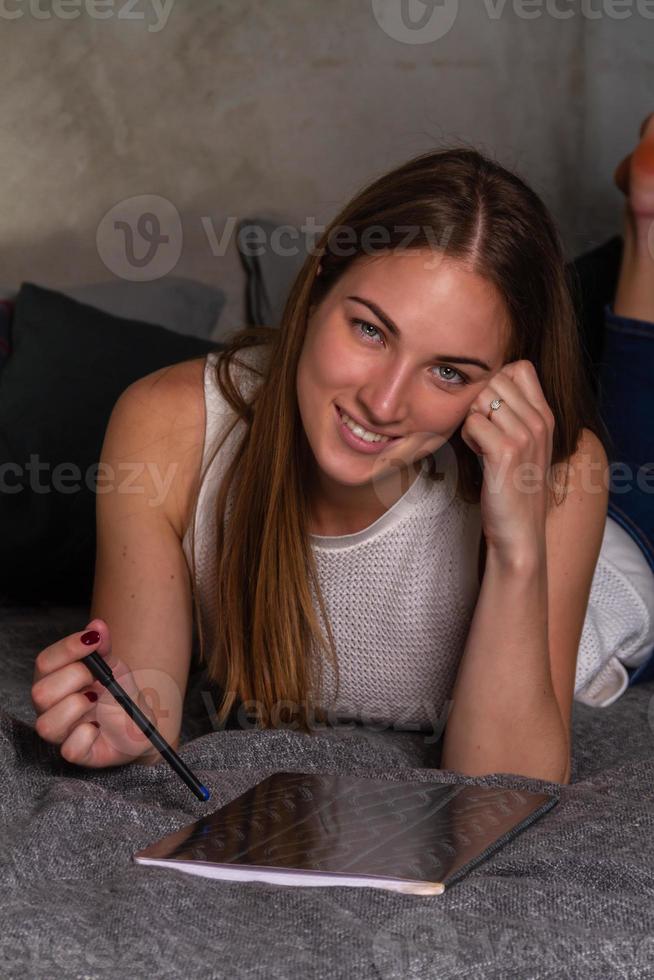 Smiling woman lying on her stomach in bed with a notebook photo