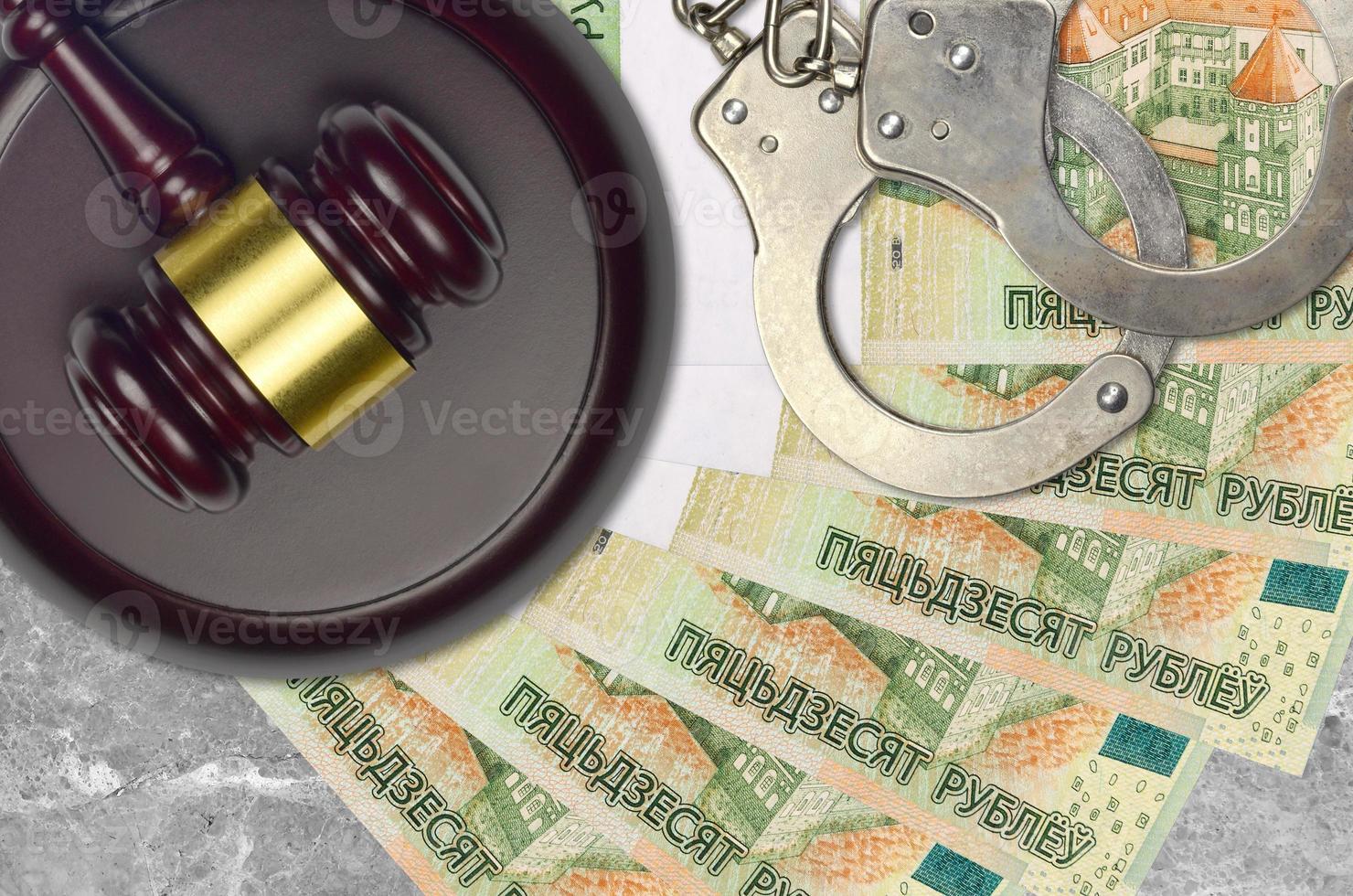 50 Belorussian rubles bills and judge hammer with police handcuffs on court desk. Concept of judicial trial or bribery. Tax avoidance photo