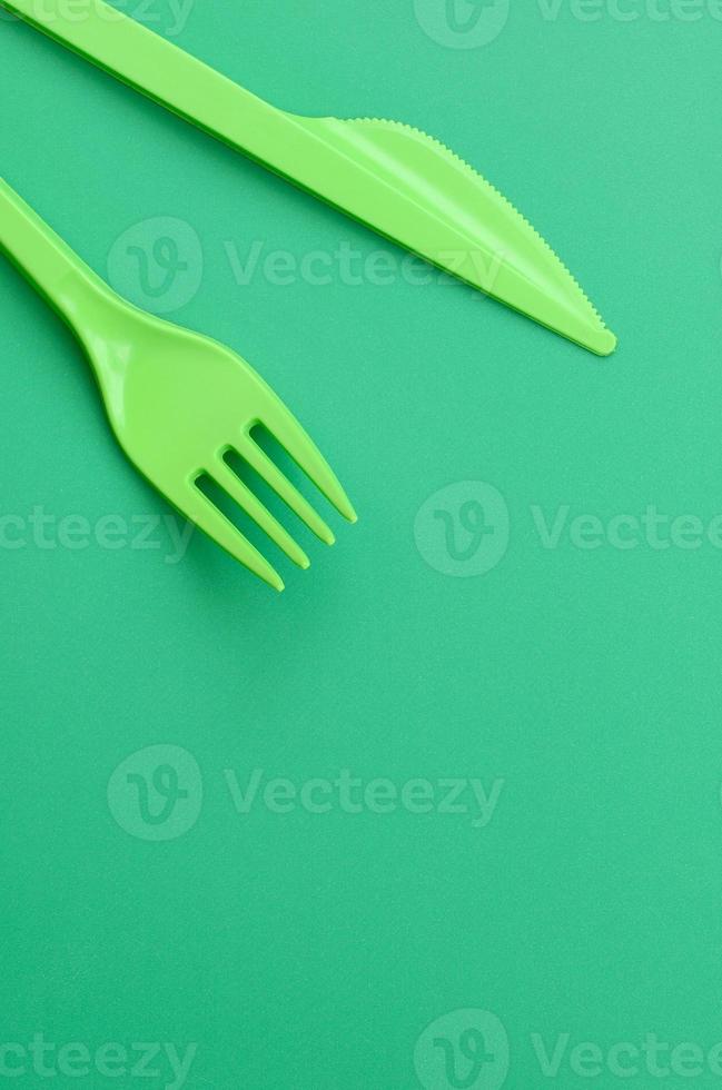 Disposable plastic cutlery green. Plastic fork and knife lie on a green background surface photo