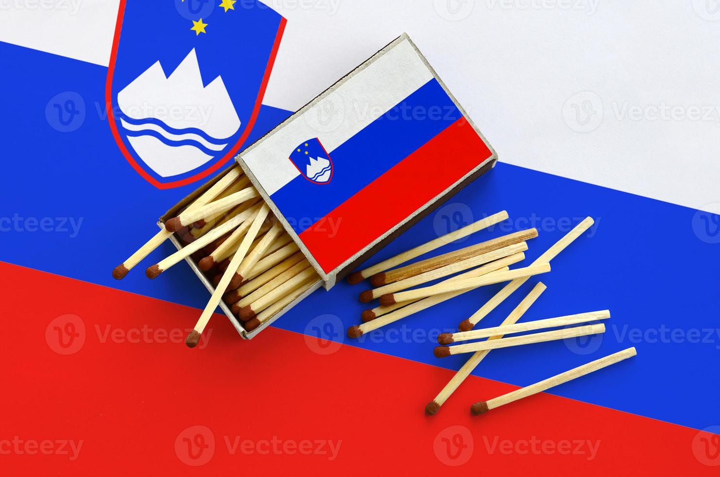 Slovenia flag is shown on an open matchbox, from which several matches fall and lies on a large flag photo