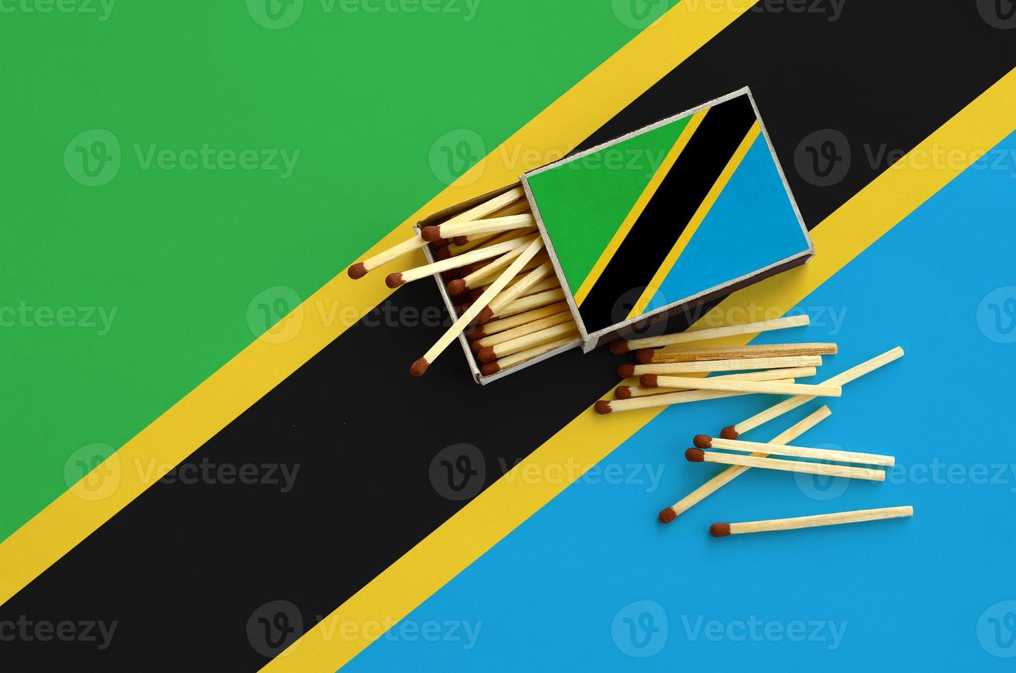 Tanzania flag is shown on an open matchbox, from which several matches fall and lies on a large flag photo