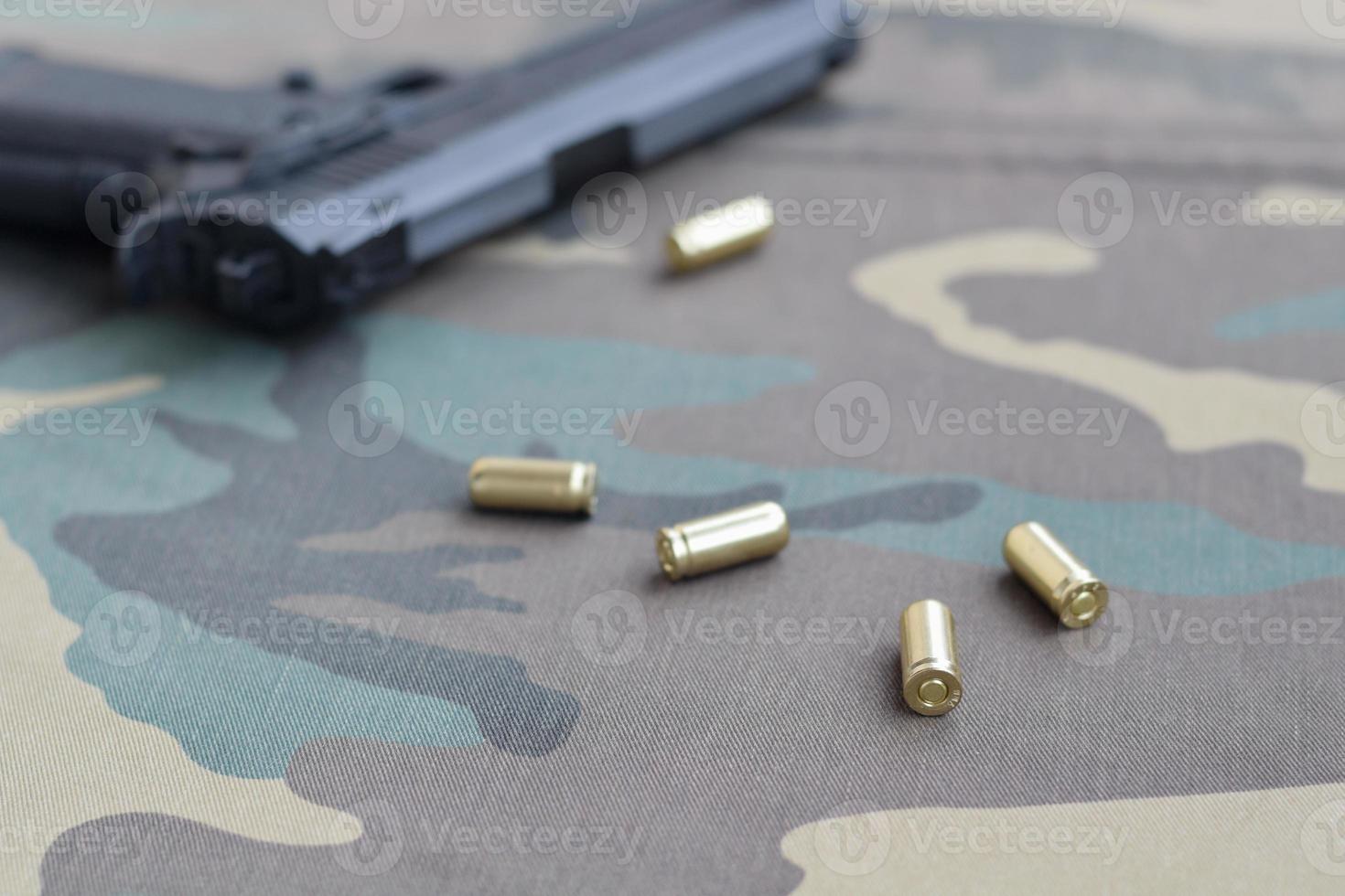9mm bullets and pistol lie on camouflage green fabric. A set shooting range items or a self-defense kit photo