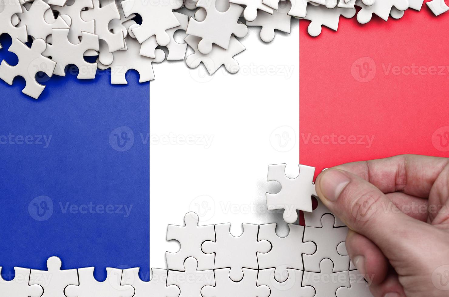France flag is depicted on a table on which the human hand folds a puzzle of white color photo