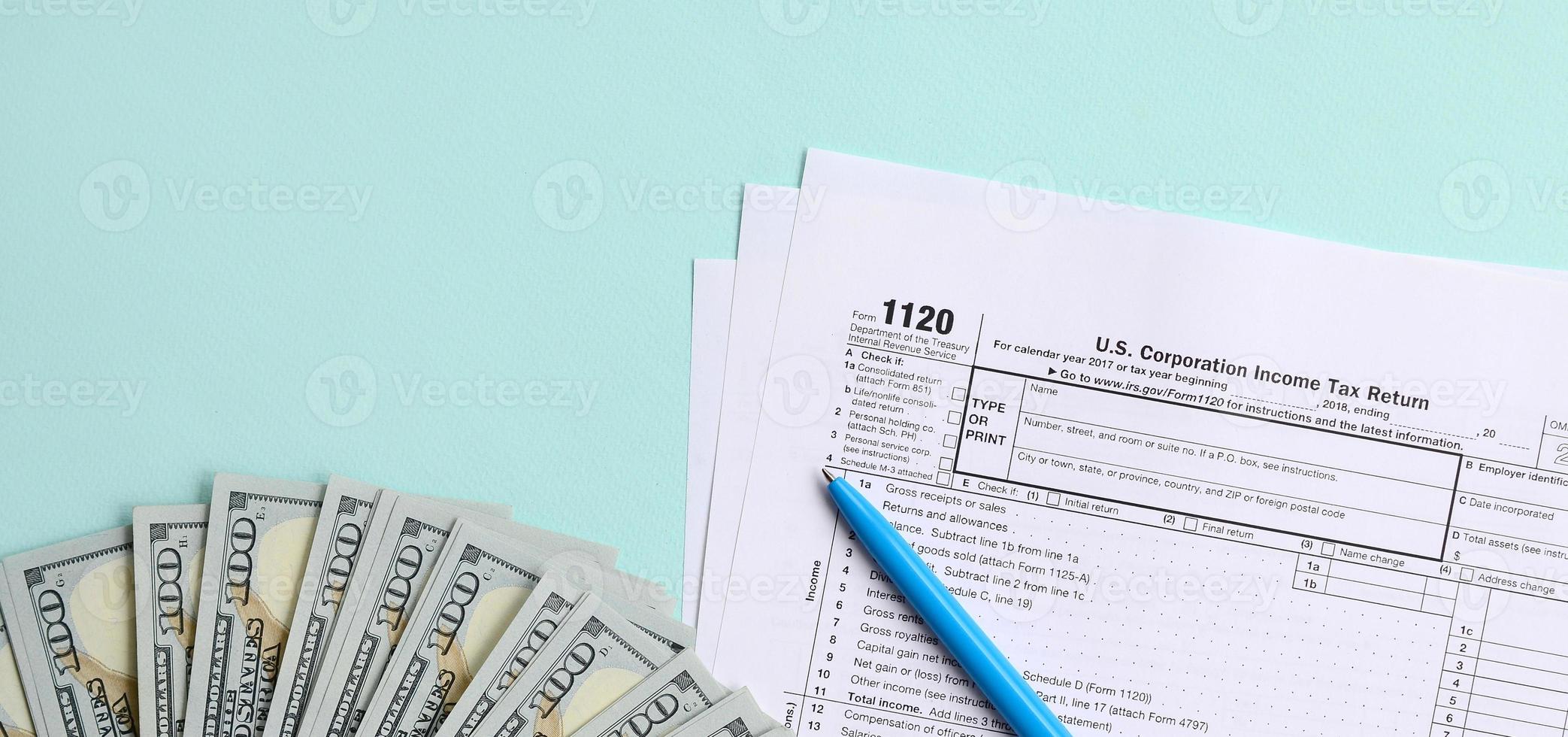 El formulario de impuestos 1120 se encuentra cerca de los billetes de cien dólares y el bolígrafo azul sobre un fondo azul claro. declaración de impuestos sobre la renta de la corporación estadounidense foto