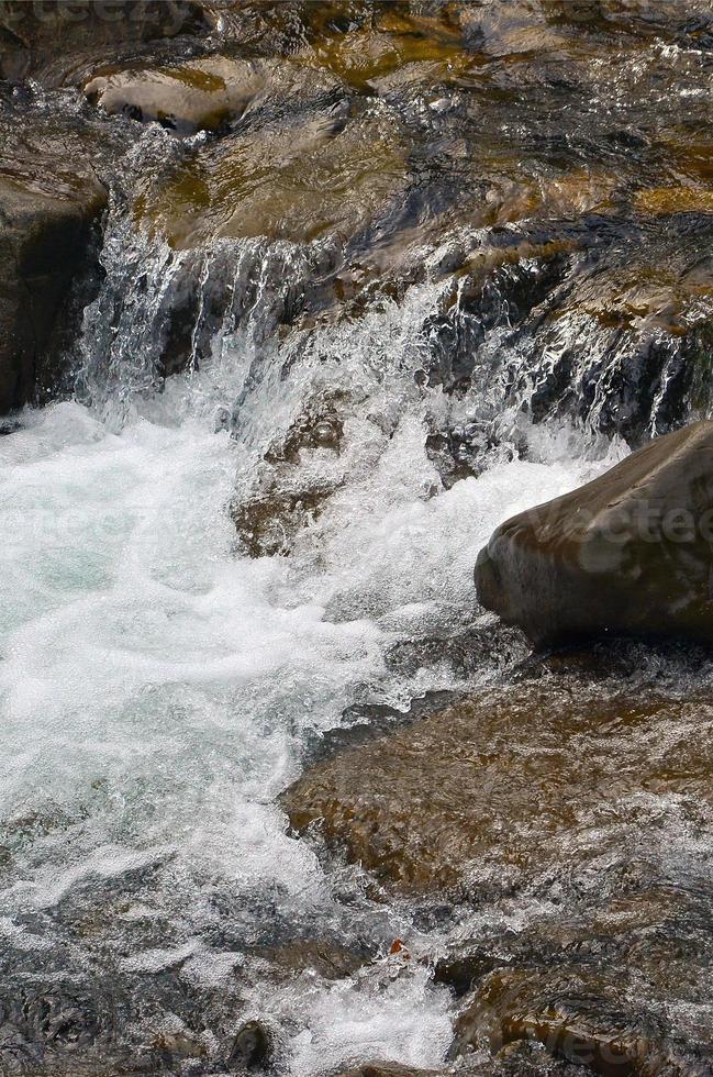 imagen de primer plano de una pequeña cascada salvaje en forma de corrientes cortas de agua entre piedras de montaña foto