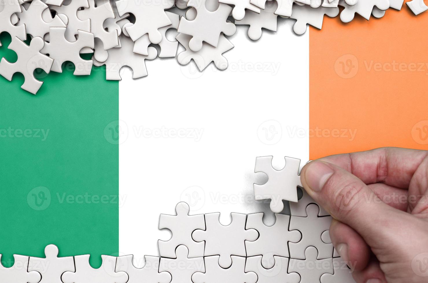 Ireland flag is depicted on a table on which the human hand folds a puzzle of white color photo