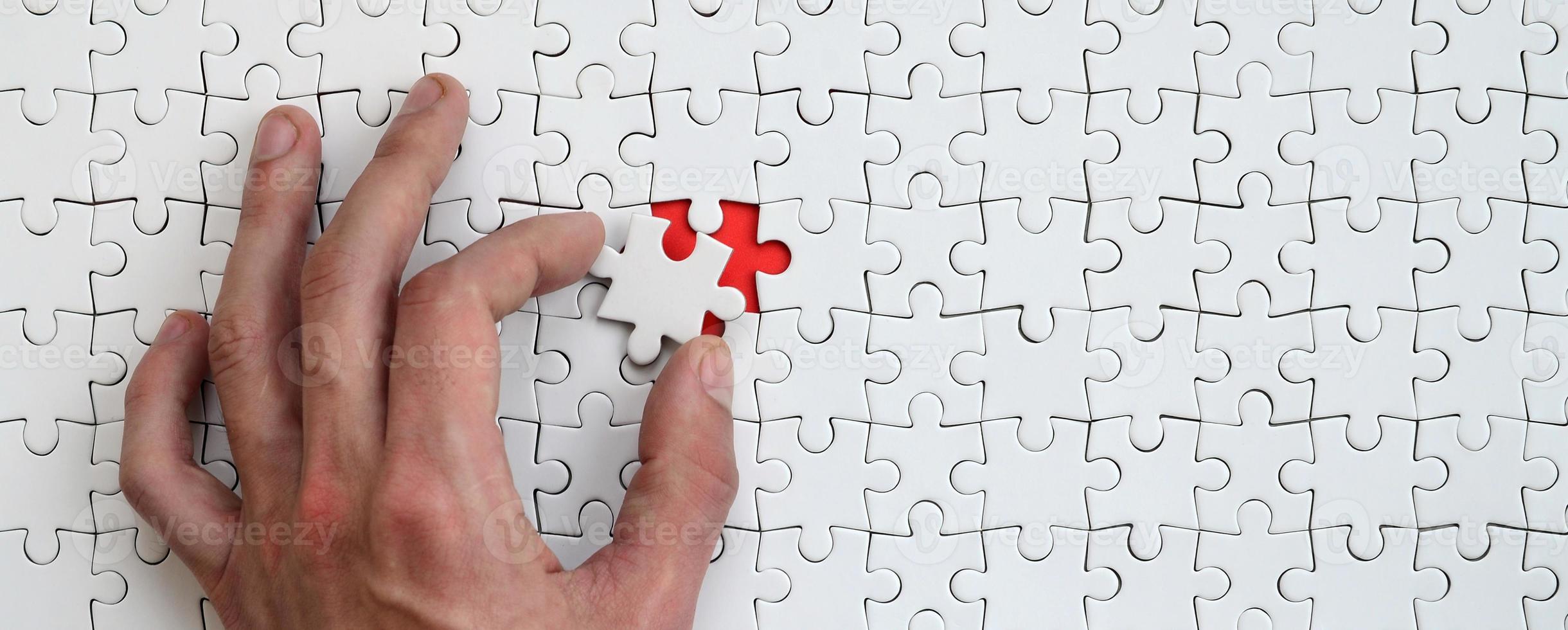 The texture of a white puzzle puzzle in the assembled state with one missing element that the male hand puts in photo