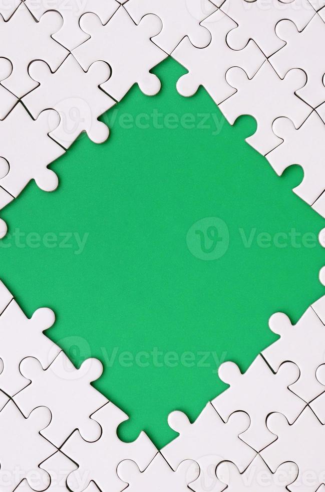 Framing in the form of a rhombus, made of a white jigsaw puzzle around the green space photo
