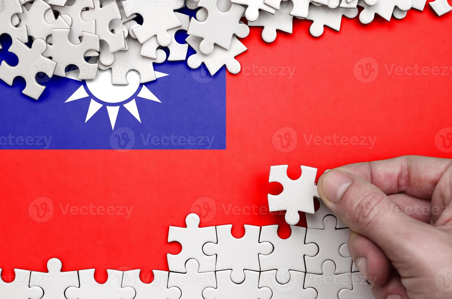 Taiwan flag is depicted on a table on which the human hand folds a puzzle of white color photo