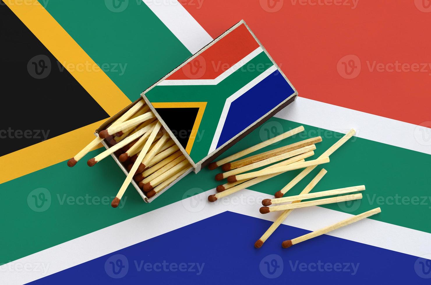 South Africa flag is shown on an open matchbox, from which several matches fall and lies on a large flag photo