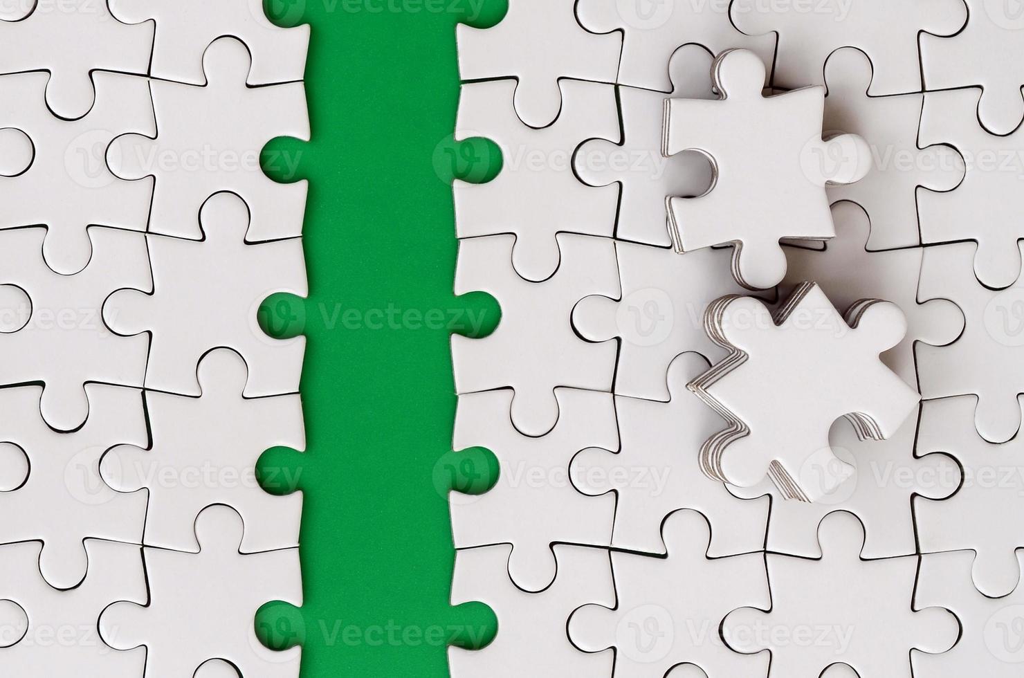 The green path is laid on the platform of a white folded jigsaw puzzle. The missing elements of the puzzle are stacked nearby. Texture image with space for text photo