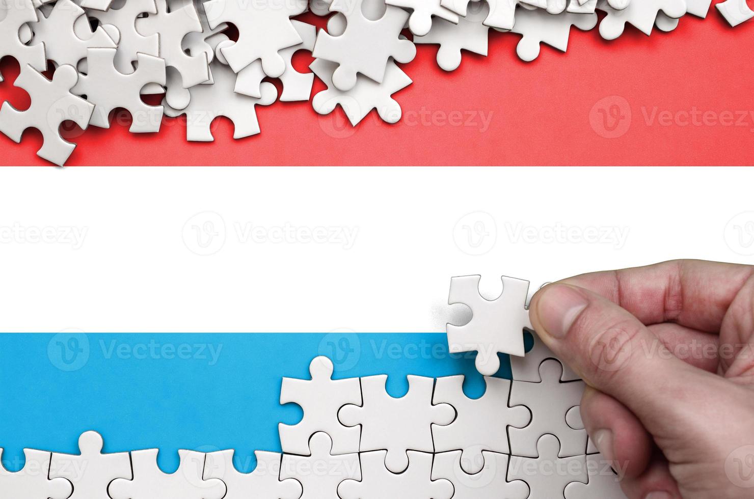 Luxembourg flag is depicted on a table on which the human hand folds a puzzle of white color photo