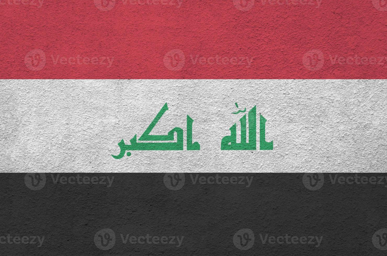 Iraq flag depicted in bright paint colors on old relief plastering wall. Textured banner on rough background photo