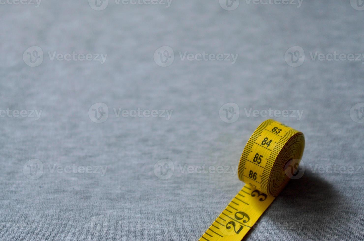 Yellow measuring tape lies on a gray knitted fabric photo