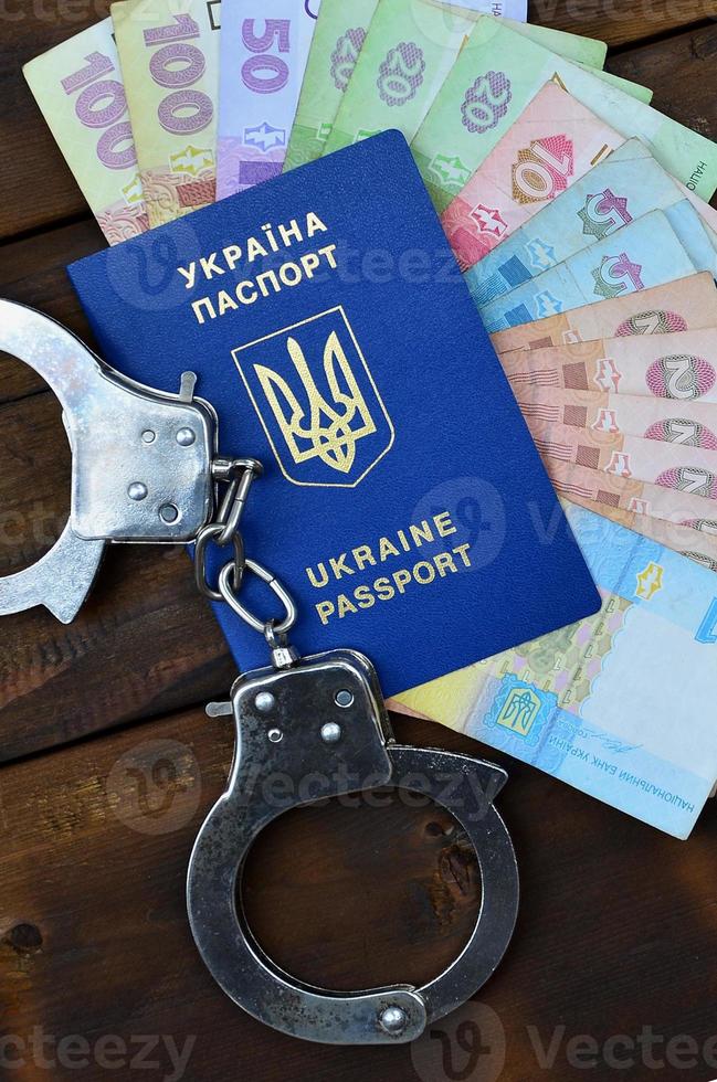 A photograph of a Ukrainian foreign passport, a certain amount of Ukrainian money and police handcuffs. Concept of illegal earnings of Ukrainian citizens abroad photo