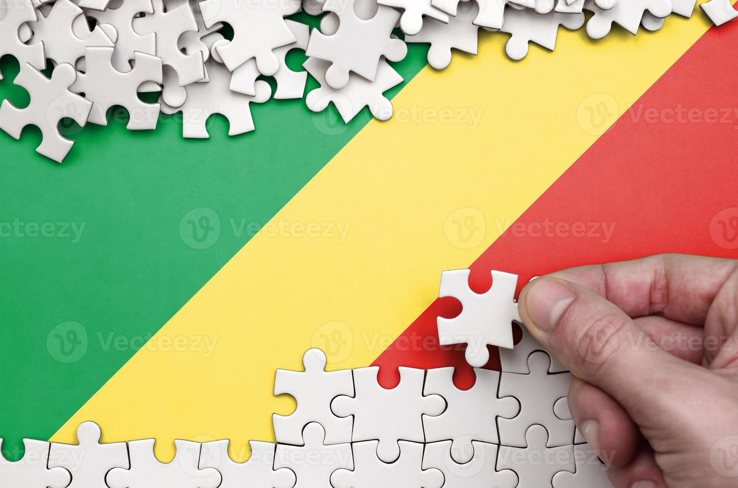 Congo flag is depicted on a table on which the human hand folds a puzzle of white color photo