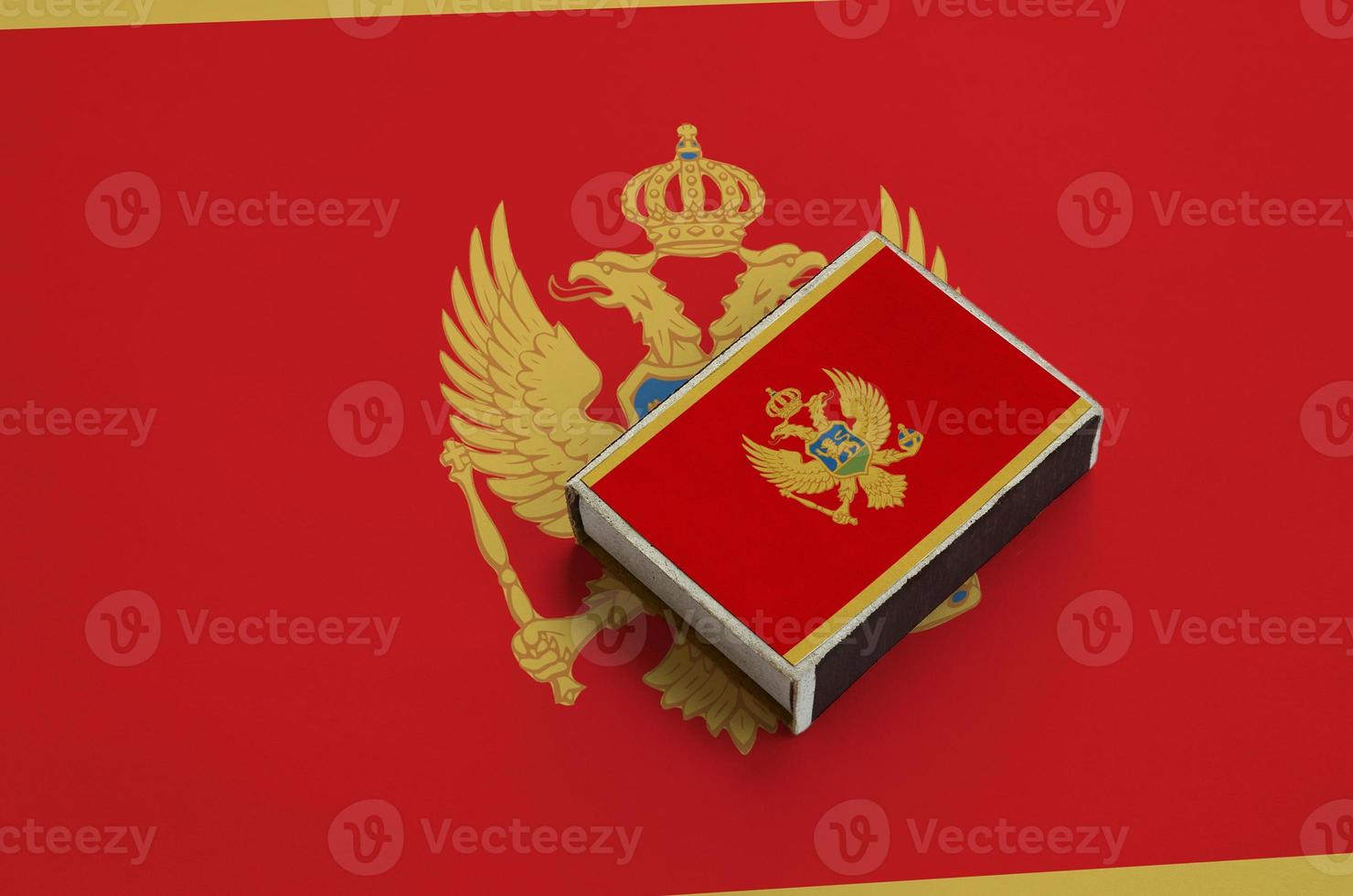 Montenegro flag is pictured on a matchbox that lies on a large flag photo