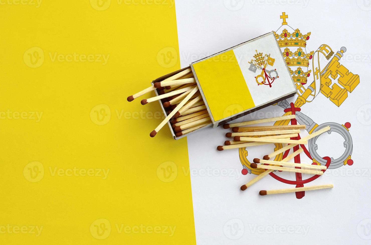 Vatican City State flag is shown on an open matchbox, from which several matches fall and lies on a large flag photo