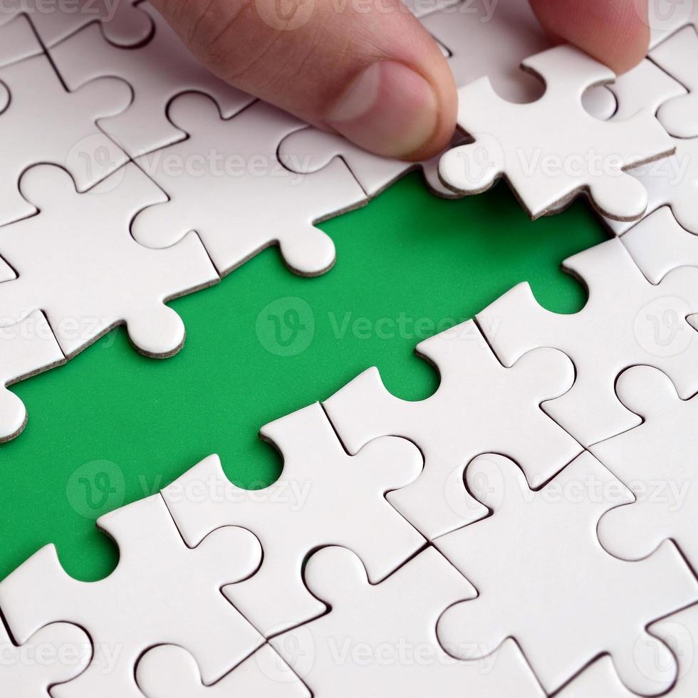 The human hand paves the way to the surface of the jigsaw puzzle, forming a green space. The concept of overcoming the difficulties on the way to success photo