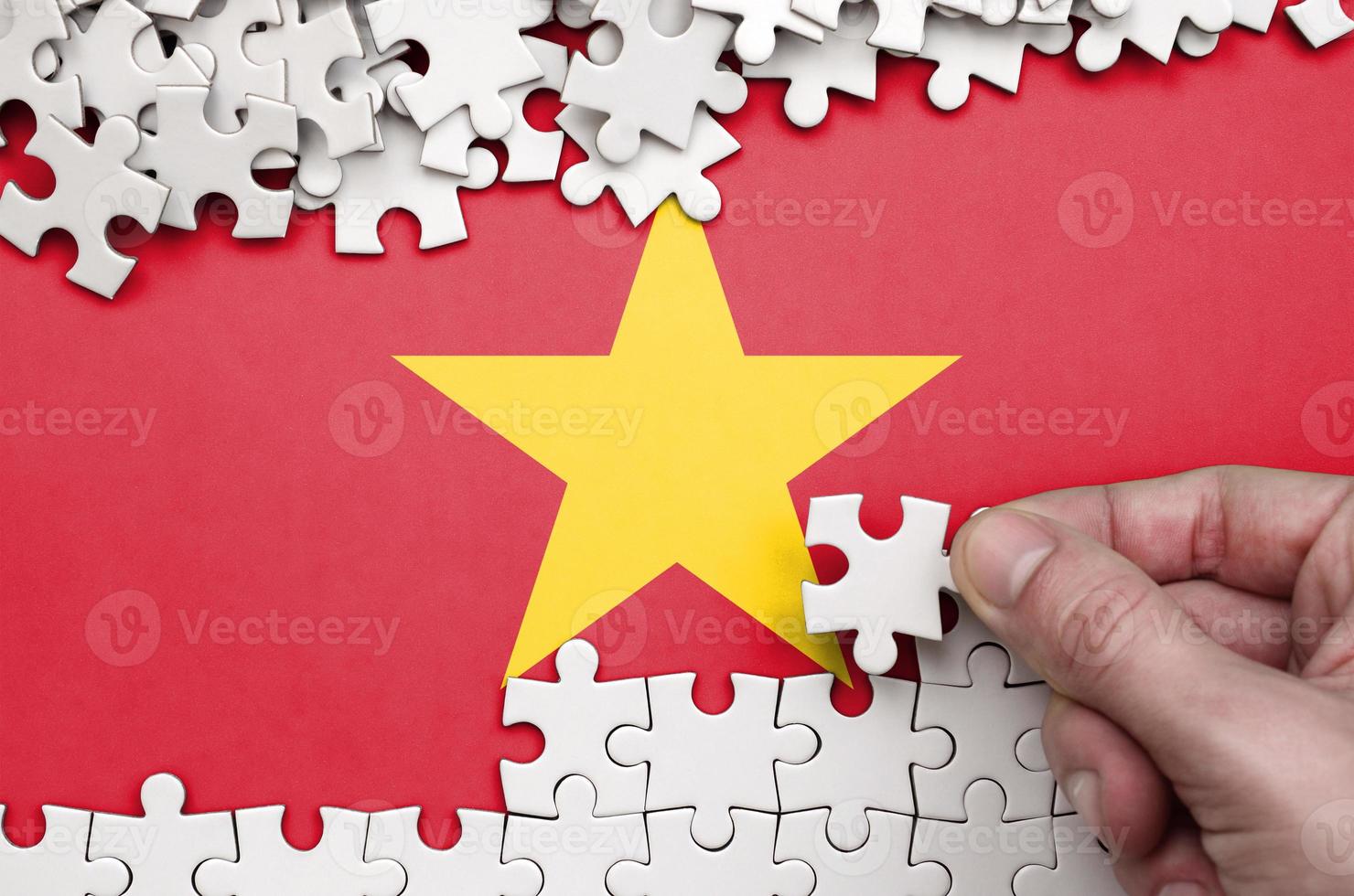 Vietnam flag is depicted on a table on which the human hand folds a puzzle of white color photo