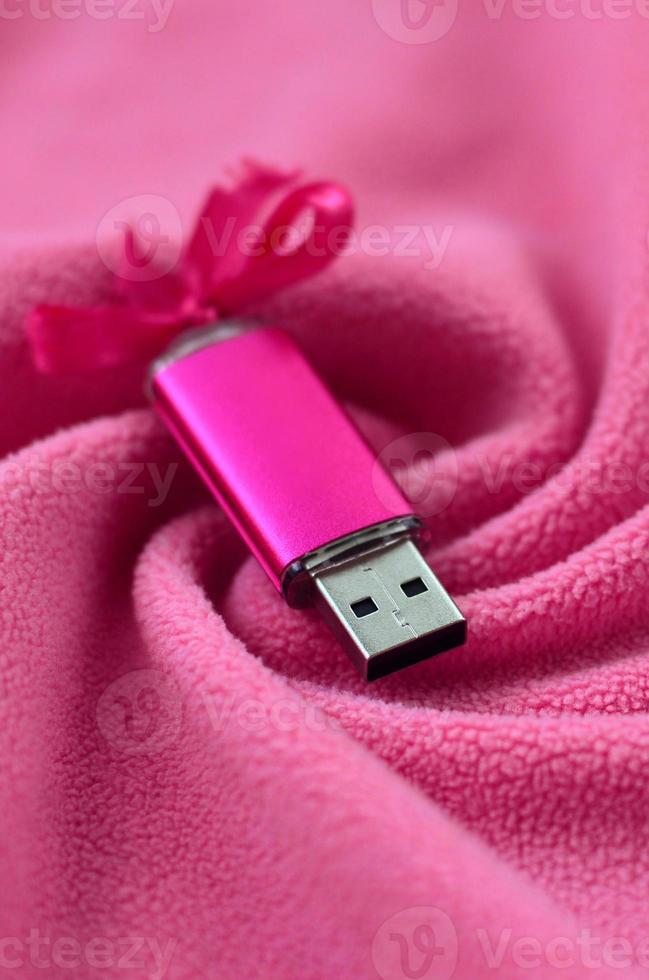 Brilliant pink usb flash memory card with a pink bow lies on a blanket of soft and furry light pink fleece fabric with a lot of relief folds. Memory storage device in women's design photo
