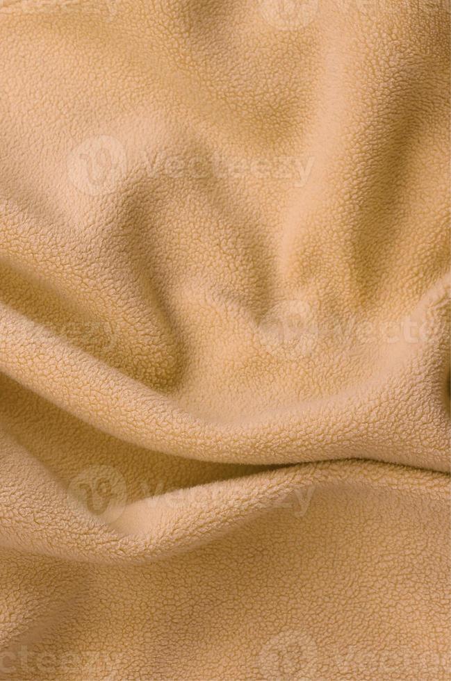 The blanket of furry orange fleece fabric. A background of light orange soft plush fleece material with a lot of relief folds photo